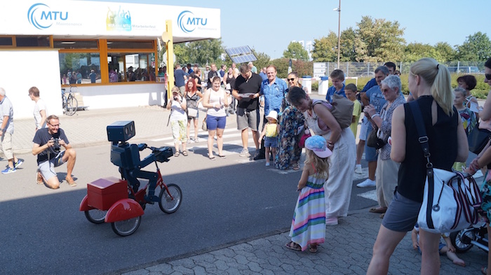 Idee Mitarbeiterfest sprechender Roboter Hugo auf Fahrrad Eingang Begrüßung